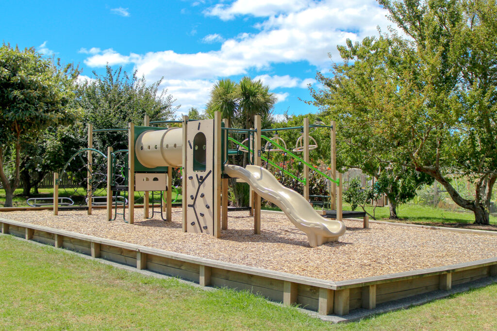 A wide view of the playground equipment designed and installed by Park Supplies & Playgrounds at Marinich Reserve, showcasing a tunnel, climbing wall, slide, and overhead bars on a wood chip surface.