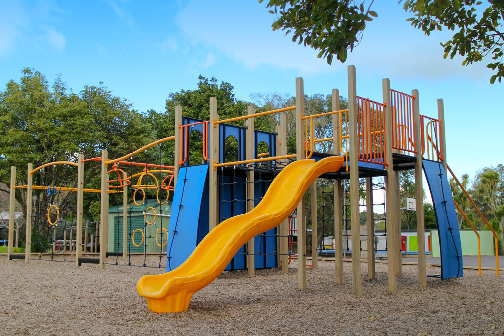 A large playground with a yellow slide and climbing activities for children, part of the high-quality playground equipment nz installed by Park Supplies & Playgrounds
